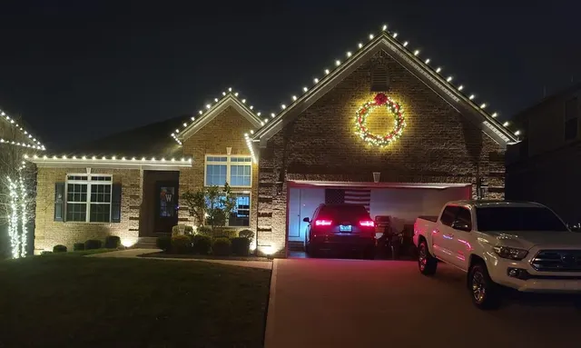 Illuminated wreath and Christmas roofline lights above a garage