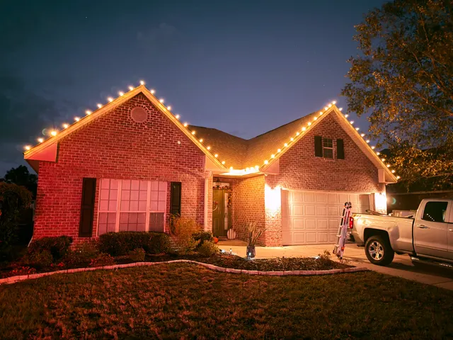 Warm roofline lights on a brick home at dusk