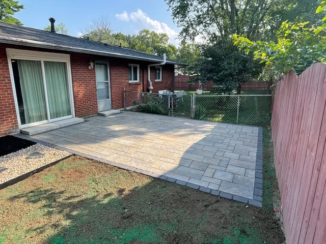 Backyard paver patio beside a brick home and wood fence